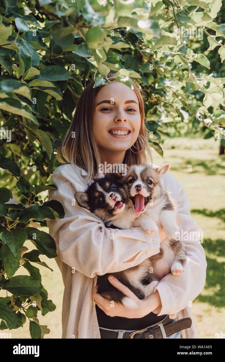 happy blonde girl holding cute puppies in garden near green tree Stock Photo