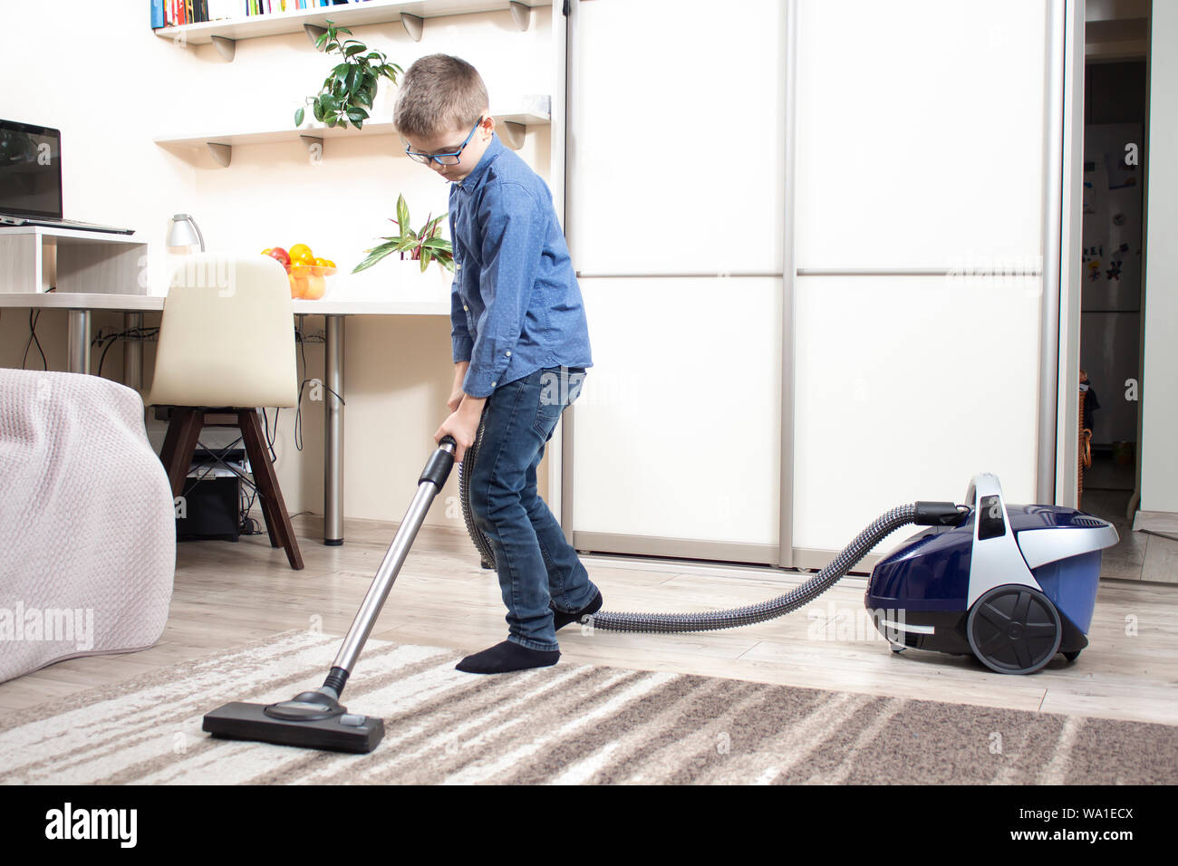 The boy in the glasses cleans the room. Vacuuming the carpet with a ...