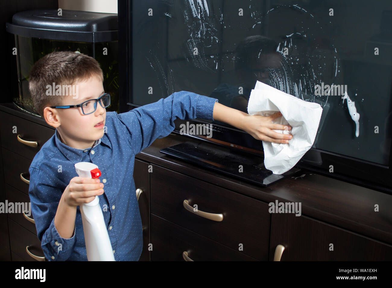 Boy with glasses during cleaning. He wipes the TV screen with dust from the cloth. Stock Photo