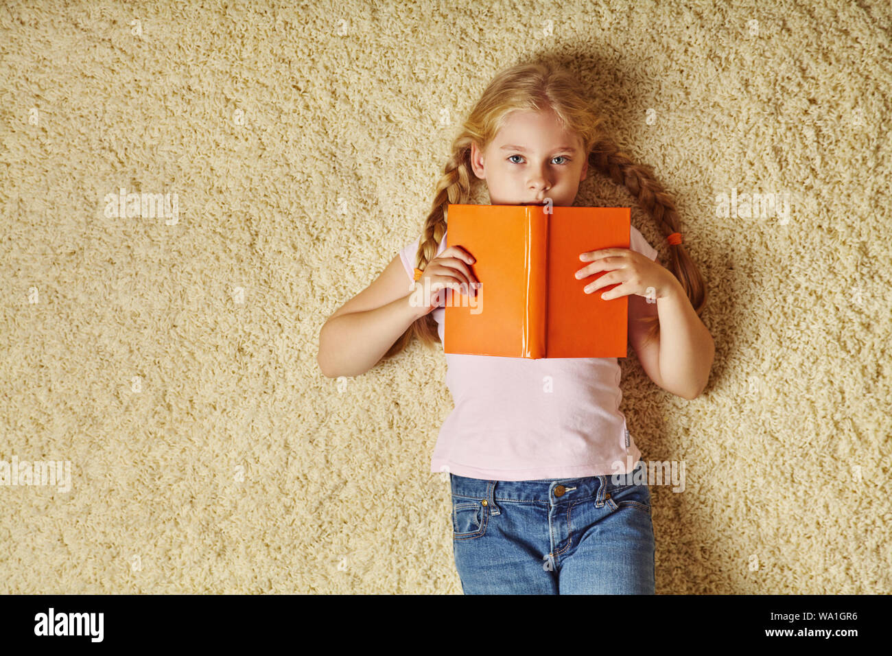 school age girl lying on a carpet with a book top view. child at home Stock Photo