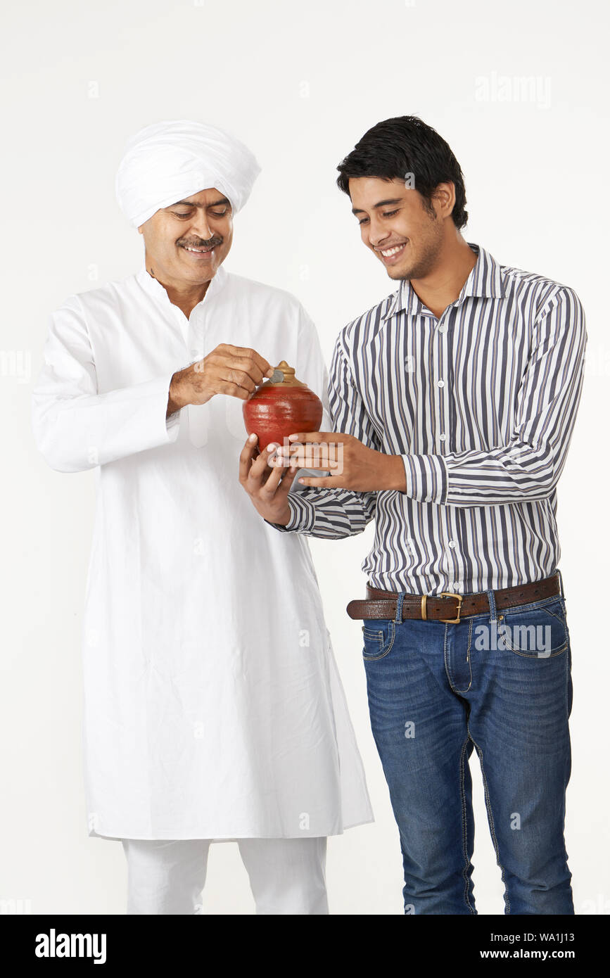 Old man putting coin into a piggy bank with his son Stock Photo - Alamy