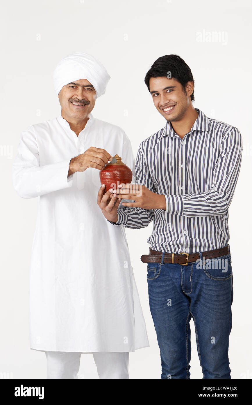 Old man putting coin into a piggy bank with his son Stock Photo - Alamy
