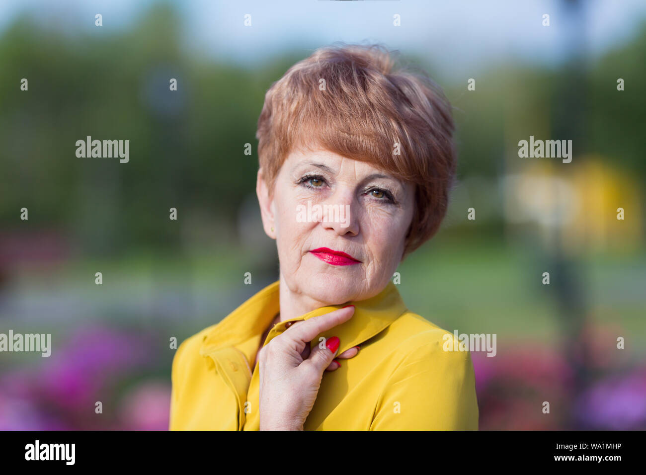Beautiful elderly woman in yellow clothes in a city park Stock Photo