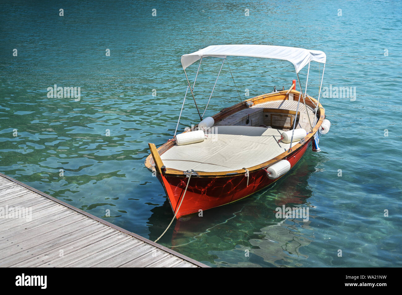 Red wooden boat with lying surface and sun canopy on the jetty in