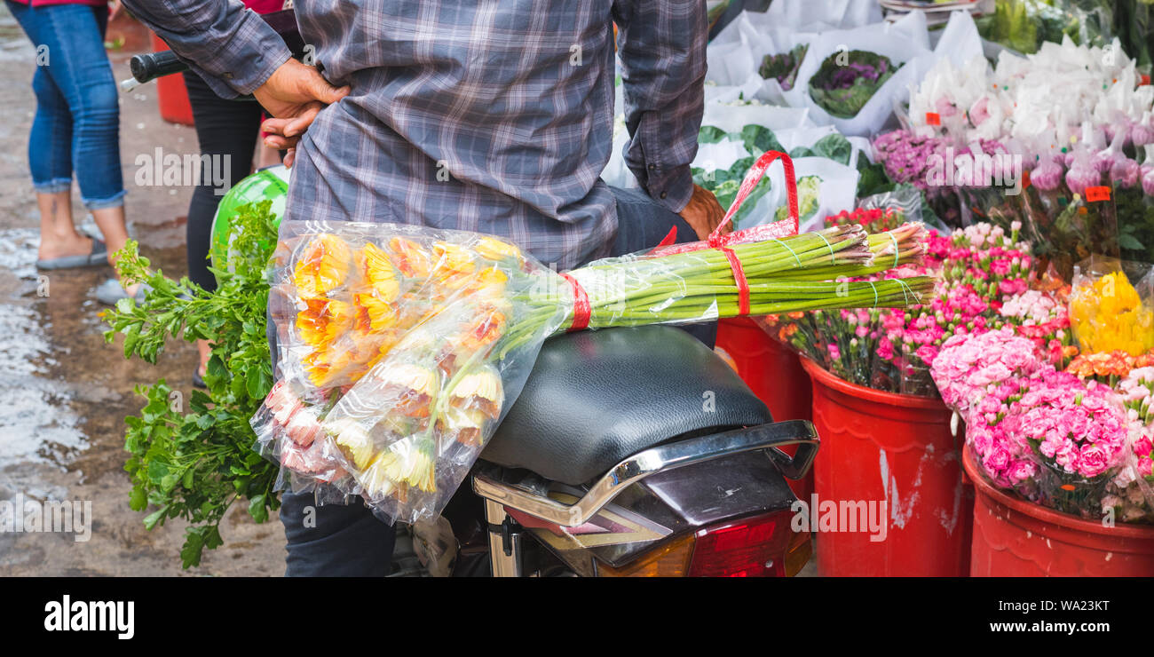 Ho Thi Ky Flower Market in Ho Chi Minh City (Saigon), Vietnam: a bouquet of flowers on a scooter seat behind a man near buckets with flowers. Stock Photo