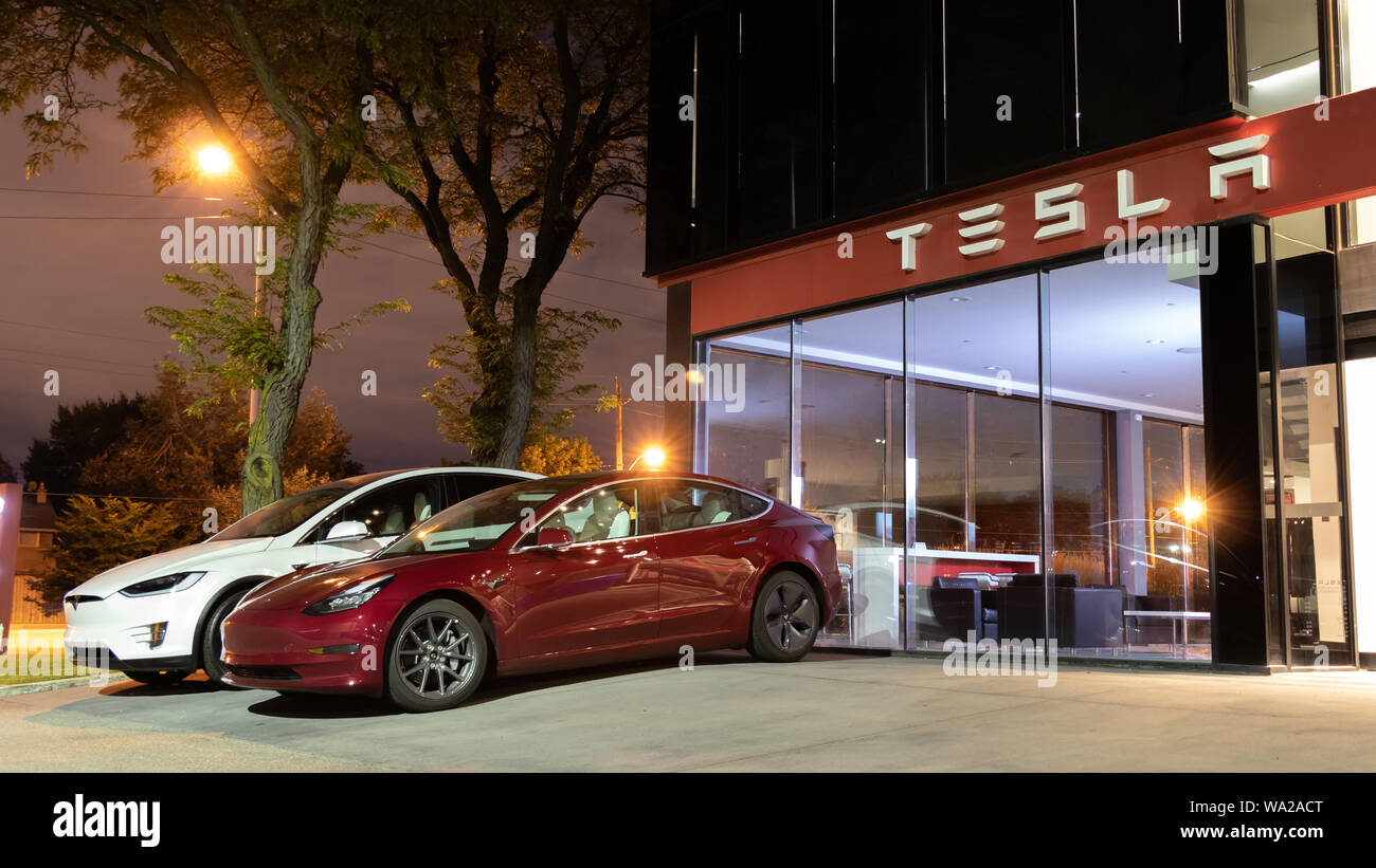 Red Tesla Model 3 and White Tesla Model X parked out-front of a Tesla Showroom at night. Stock Photo