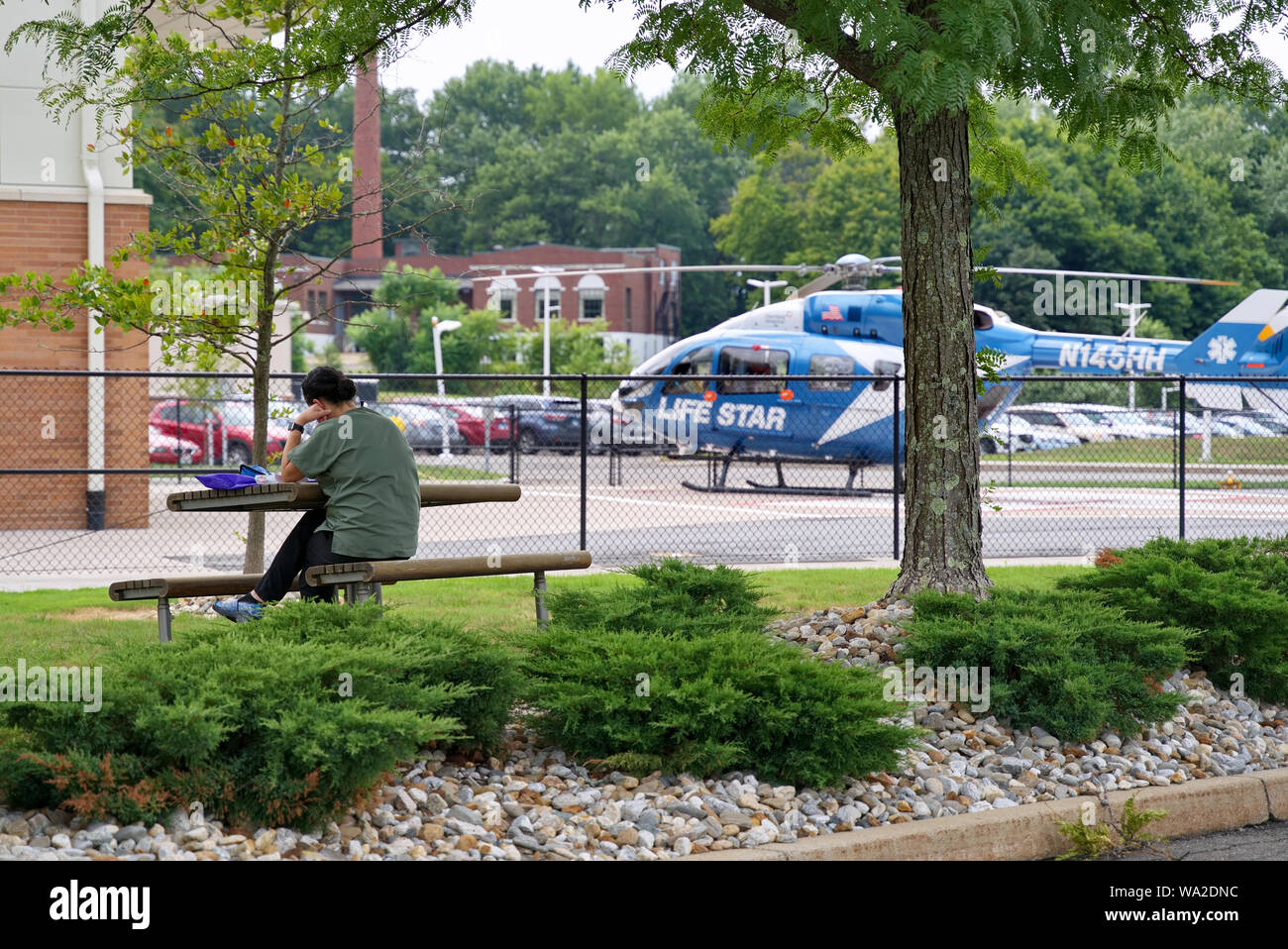 Meriden, CT USA. Aug 2019. Hospital personnel having lunch under a tree nearby the Life Star medical transport helicopter. Stock Photo