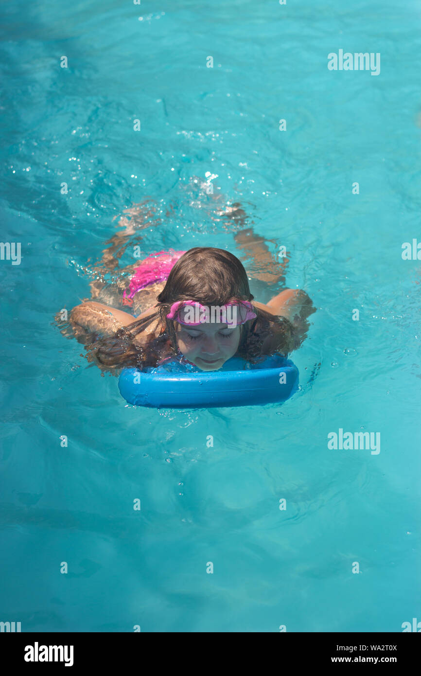 Little girl on the floating board, learns to swim in the pool Stock