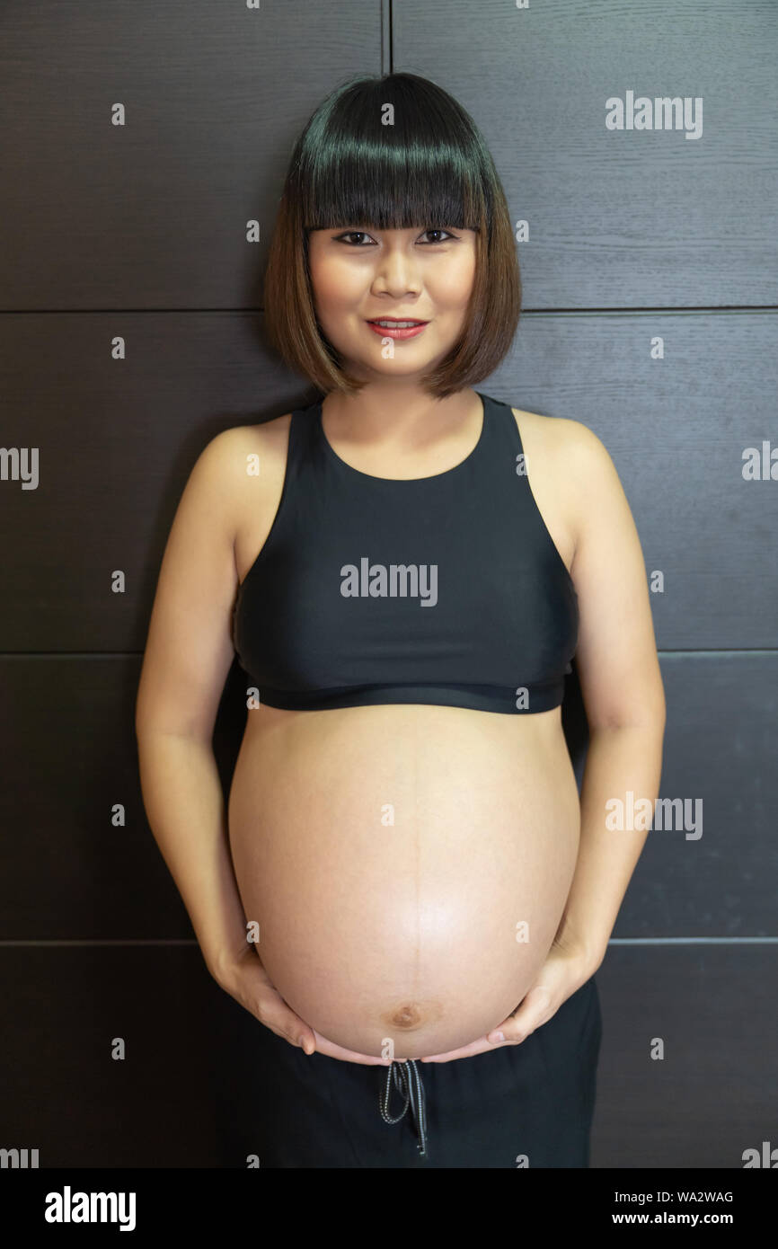 Portrait of pregnant asian woman touching her big belly happily. Stock Photo
