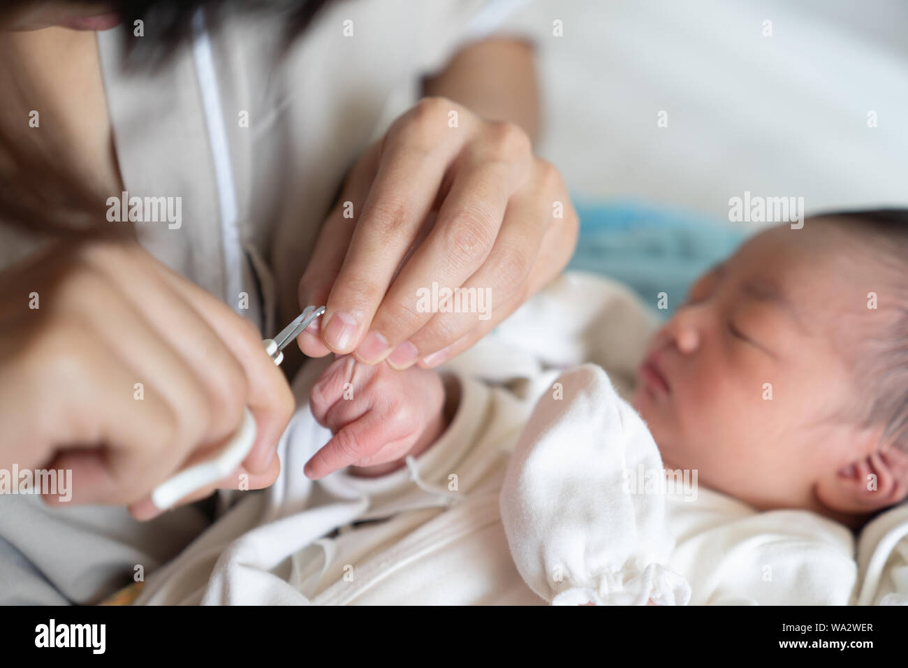 Asian baby getting fingernails cut while sleeping by his mother with scissors. Close Up Nursing a child. How to successfully clip your baby’s nails. Stock Photo