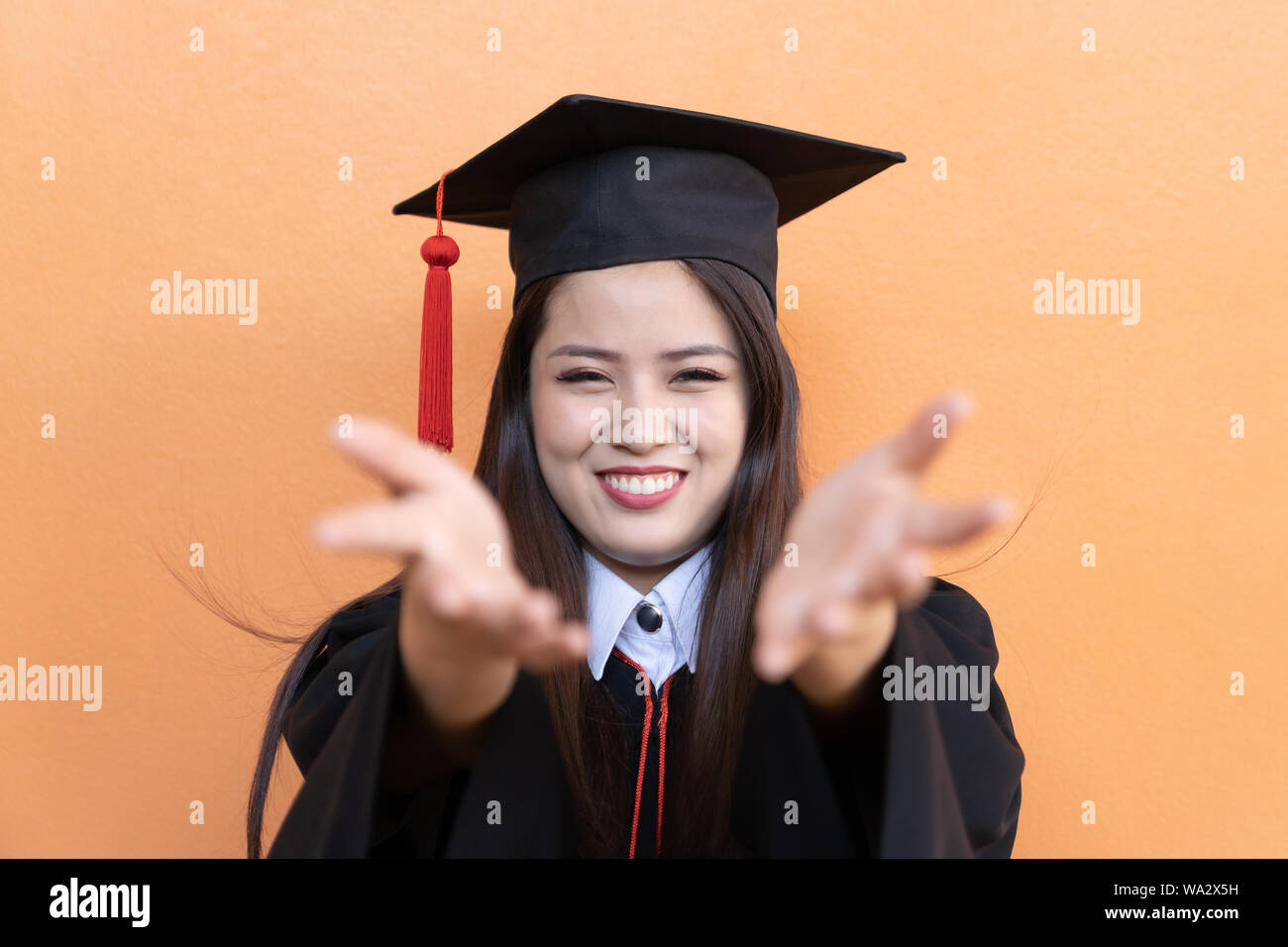 Portrait closeup. Asian beautiful smiley graduate graduated student girl young woman in cap gown on isolated orange background wall. Celebrating gradu Stock Photo