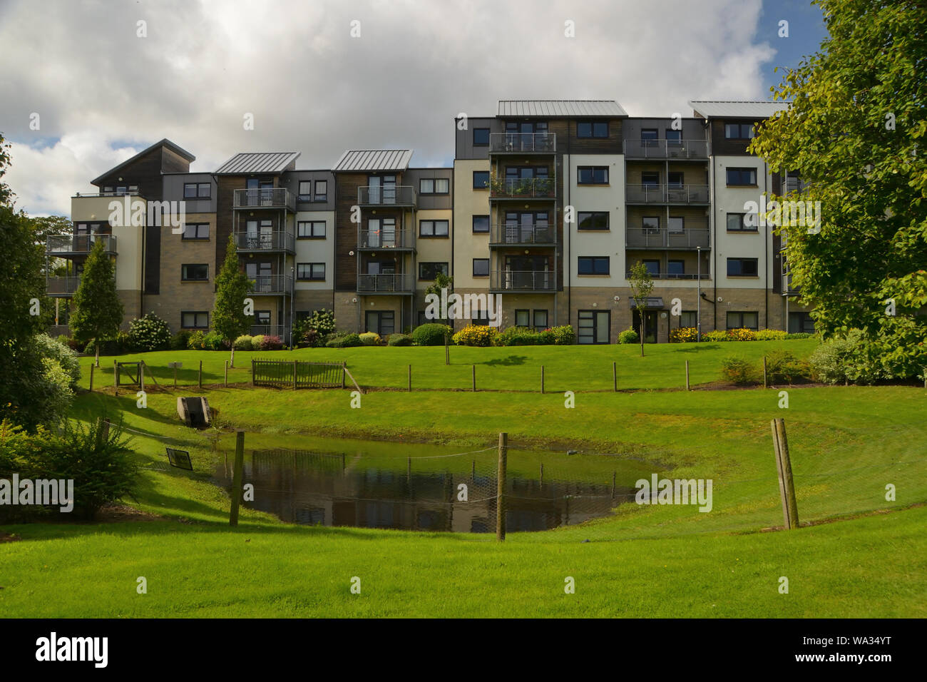 An apartment block with green landscaping and a balancing pond for sustainable drainage (a SuDS pond), at old Hilton Campus, Aberdeen, Scotland, UK. Stock Photo