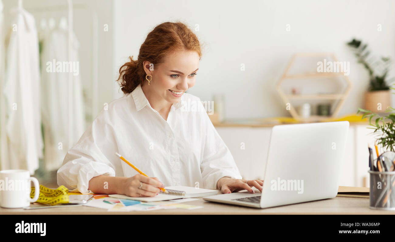 Young designer using laptop and making notes in atelier Stock Photo