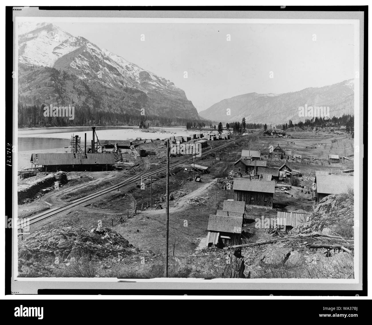Bird's-eye view of Eddy, Montana, showing buildings, railroad tracks along river, and snow-capped mountains in background Stock Photo