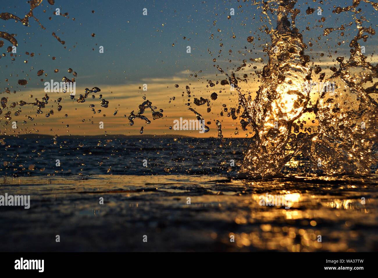 A sun-filled beach scene with a stop-action splashing wave/ Sunset at the sea Stock Photo