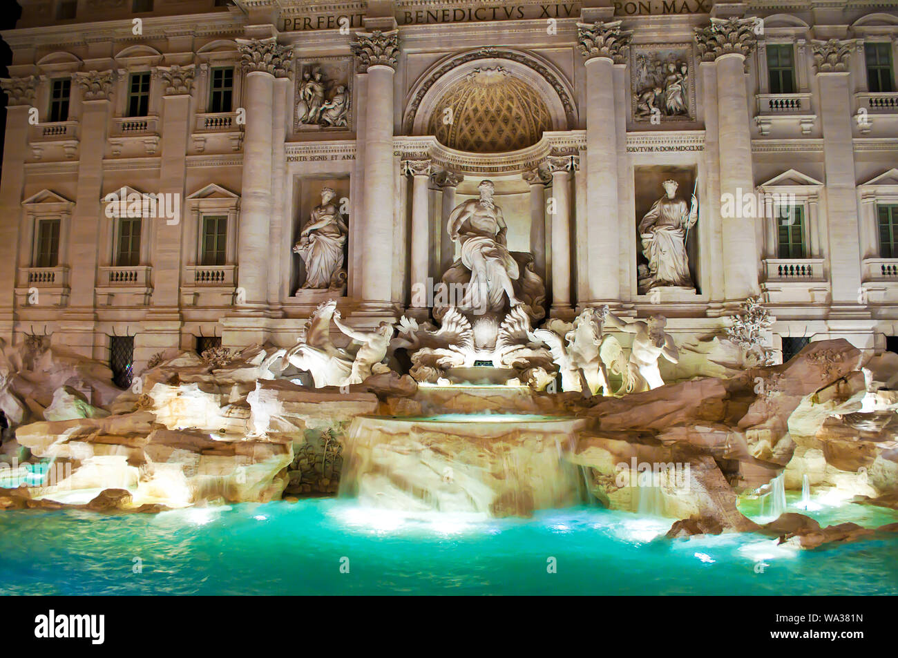View of the illuminated Fontana di Trevi and green flowing waters at night. Many intricate statues and marble columns Stock Photo