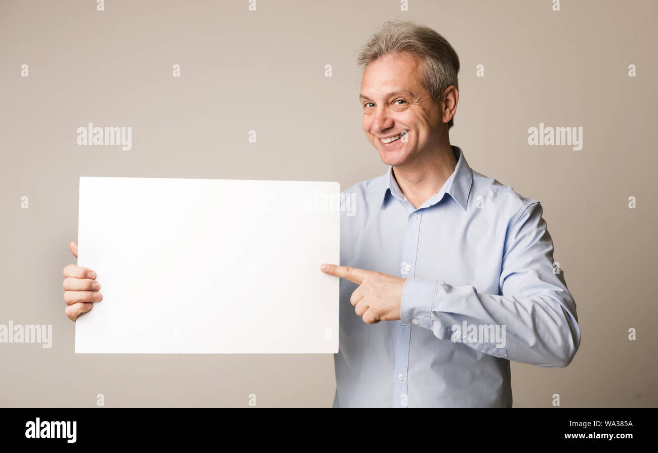 Mature man holding blank board and pointing on it Stock Photo
