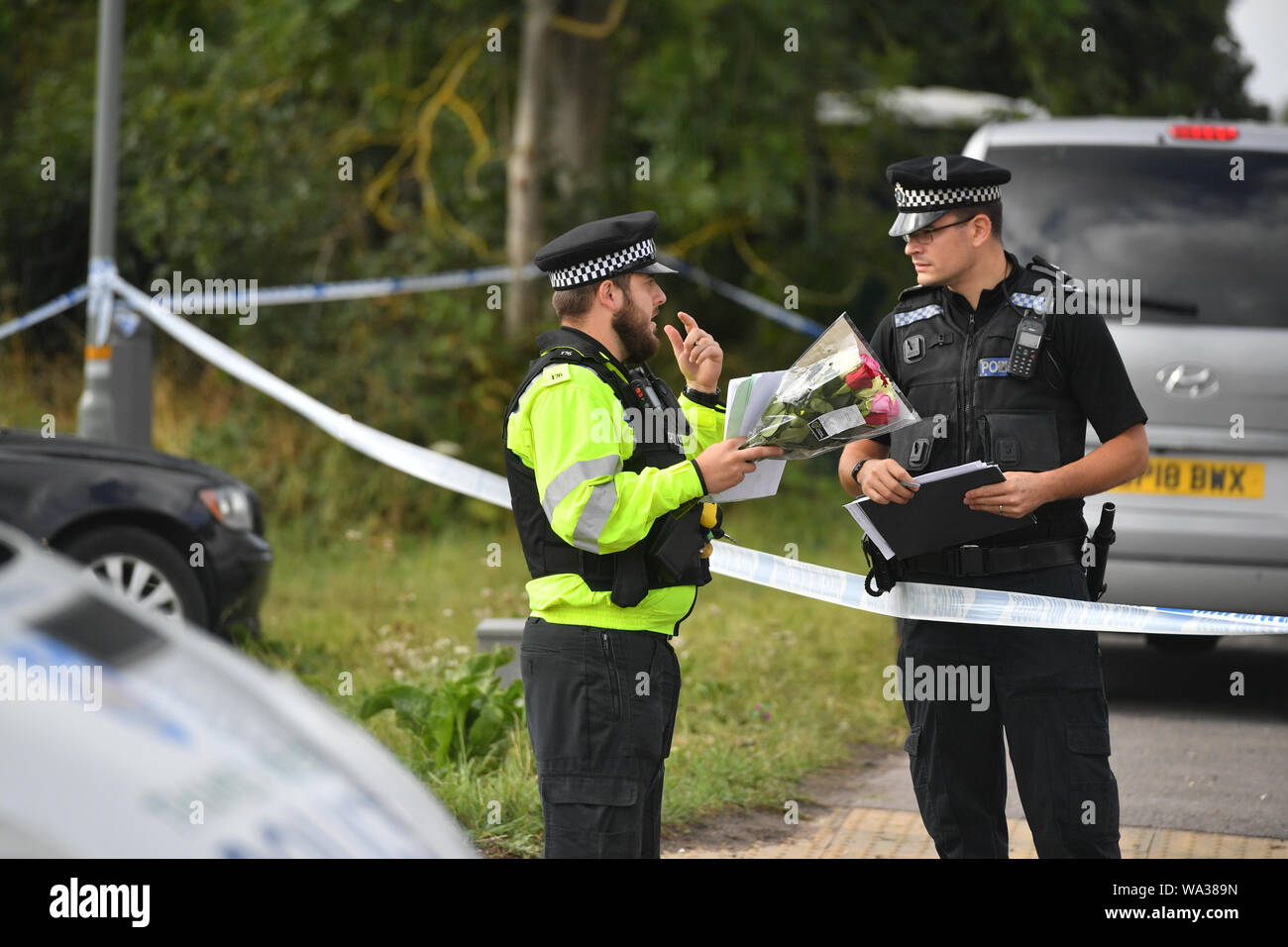 A police officer holds a floral tribute at the scene, where Thames Valley Police officer Pc Andrew Harper, 28, died following a 'serious incident' at about 11.30pm on Thursday near the A4 Bath Road, between Reading and Newbury, at the village of Sulhamstead in Berkshire. Stock Photo