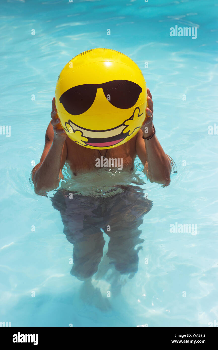 Man is making fun in the pool, having inflatable yellow ball infront of his face Stock Photo