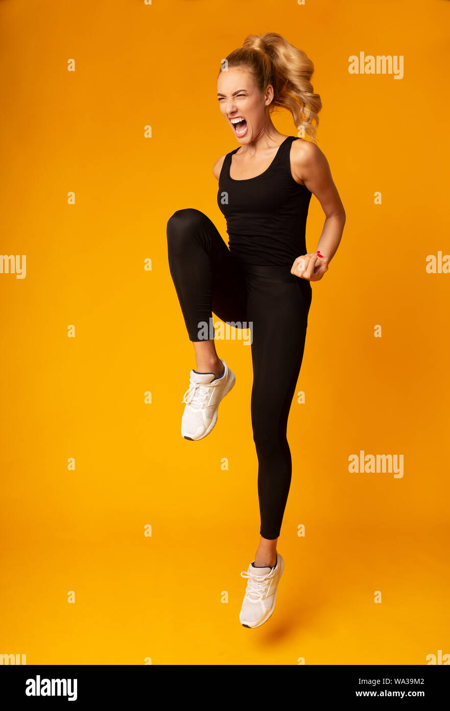 Skinny Girl Jumping Expressing Aggression Over Yellow Studio Background Stock Photo