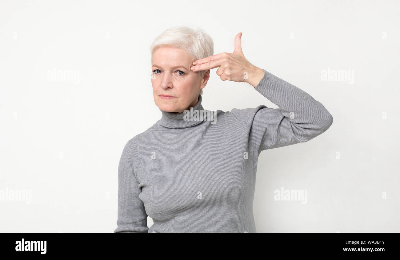 Serious senior woman committing suicide with finger gun gesture Stock Photo