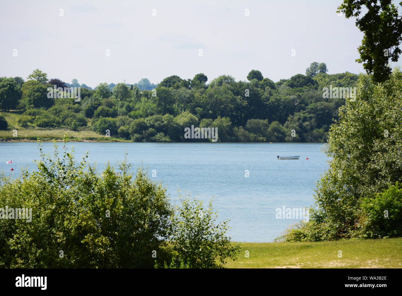 Small boat on Bewl Water reservoir in Tunbridge Wells, Kent. Verdant trees and bushes grow at the water's edge. Stock Photo
