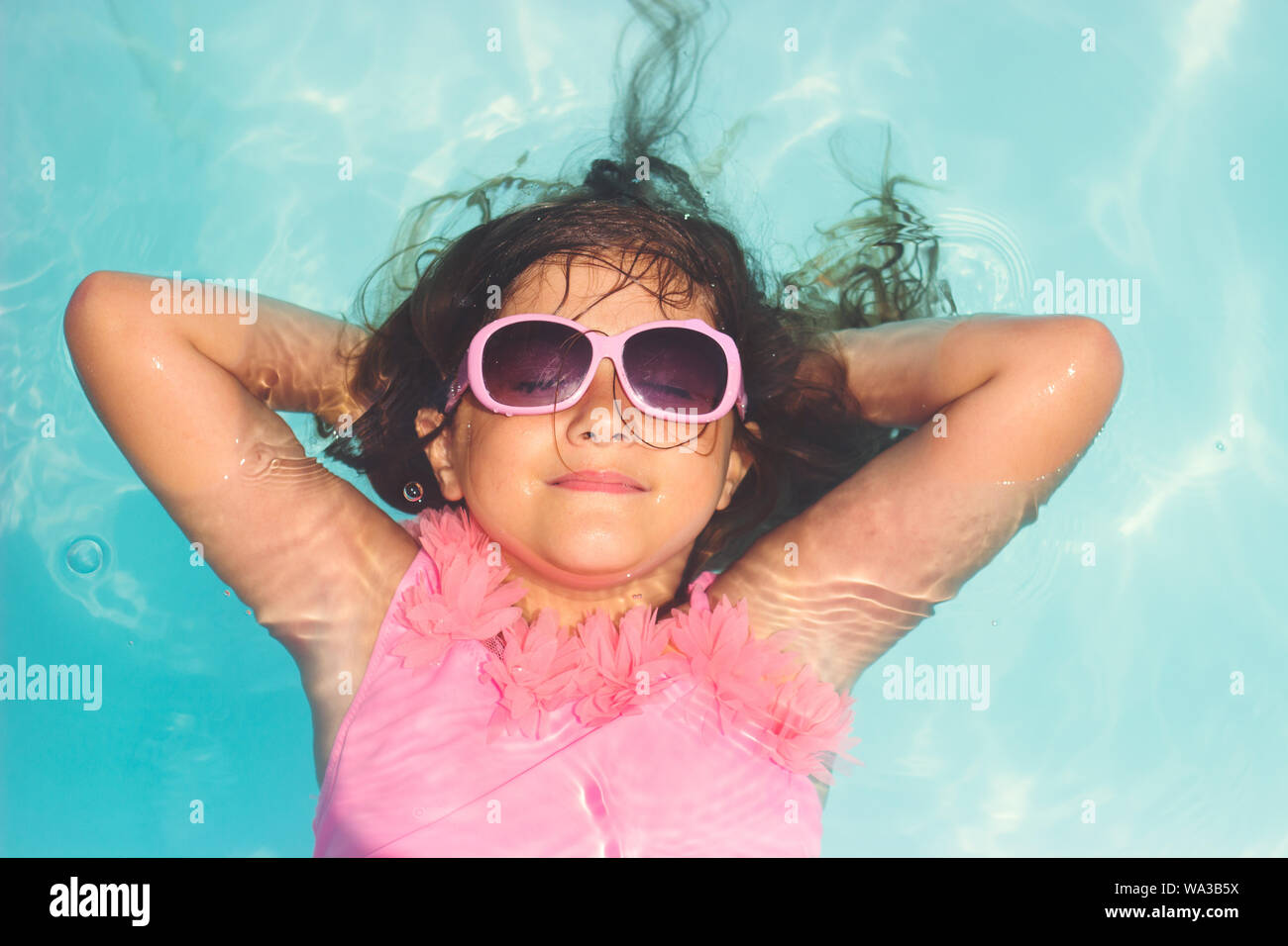 Cute little girl with pink sunglasses, smiling and laying relaxed in