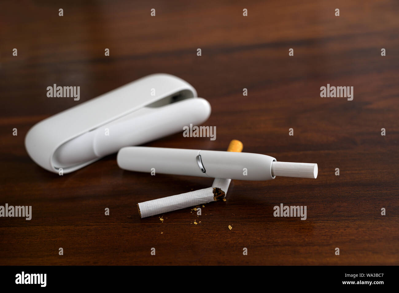 White heating tobacco system is breaking a normal cigarette on a brown table, new kind of electronic cigarette with tobacco sticks, that generates a n Stock Photo