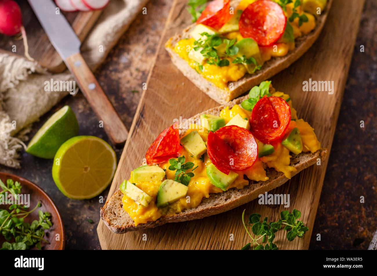Bio scrambled eggs on rustic french baguette with salami, fresh herbs