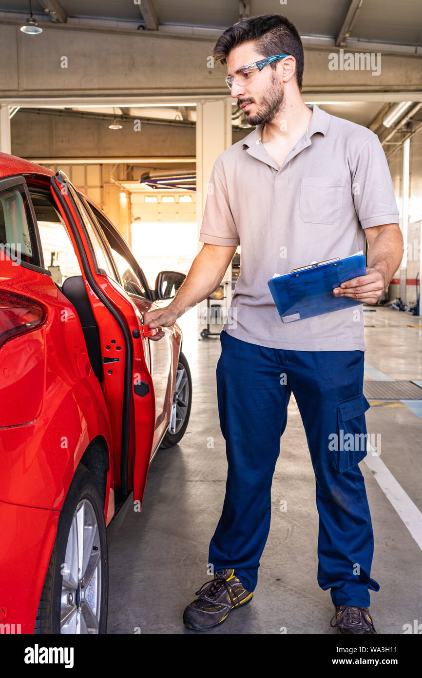 Technician with safety glasses inspecting the opening of a red car door in a vehicle inspection