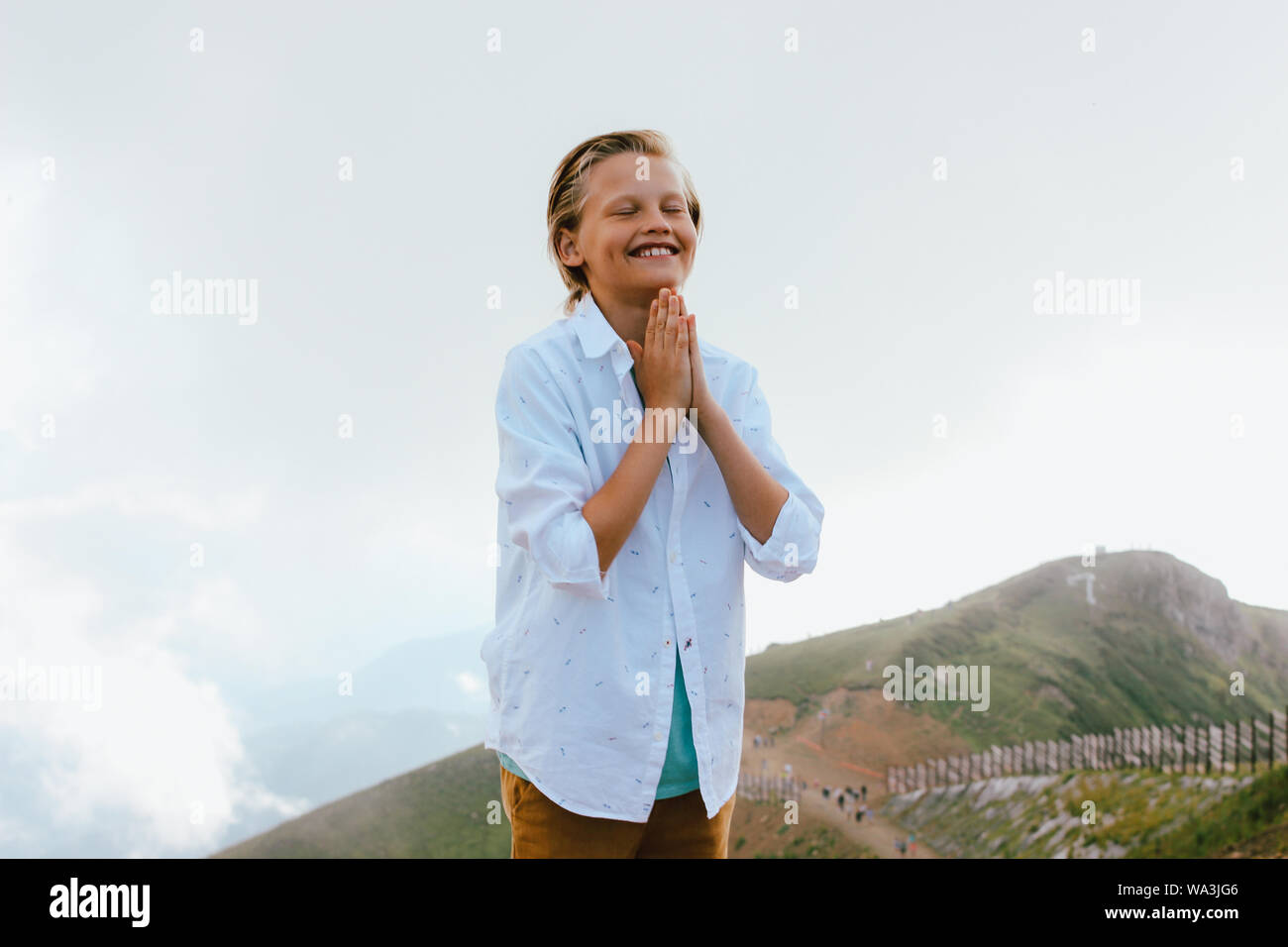 Blonde smiling boy closing eyes on background of wonderful view of the mountain resort, family travel adventure lifestyle Stock Photo