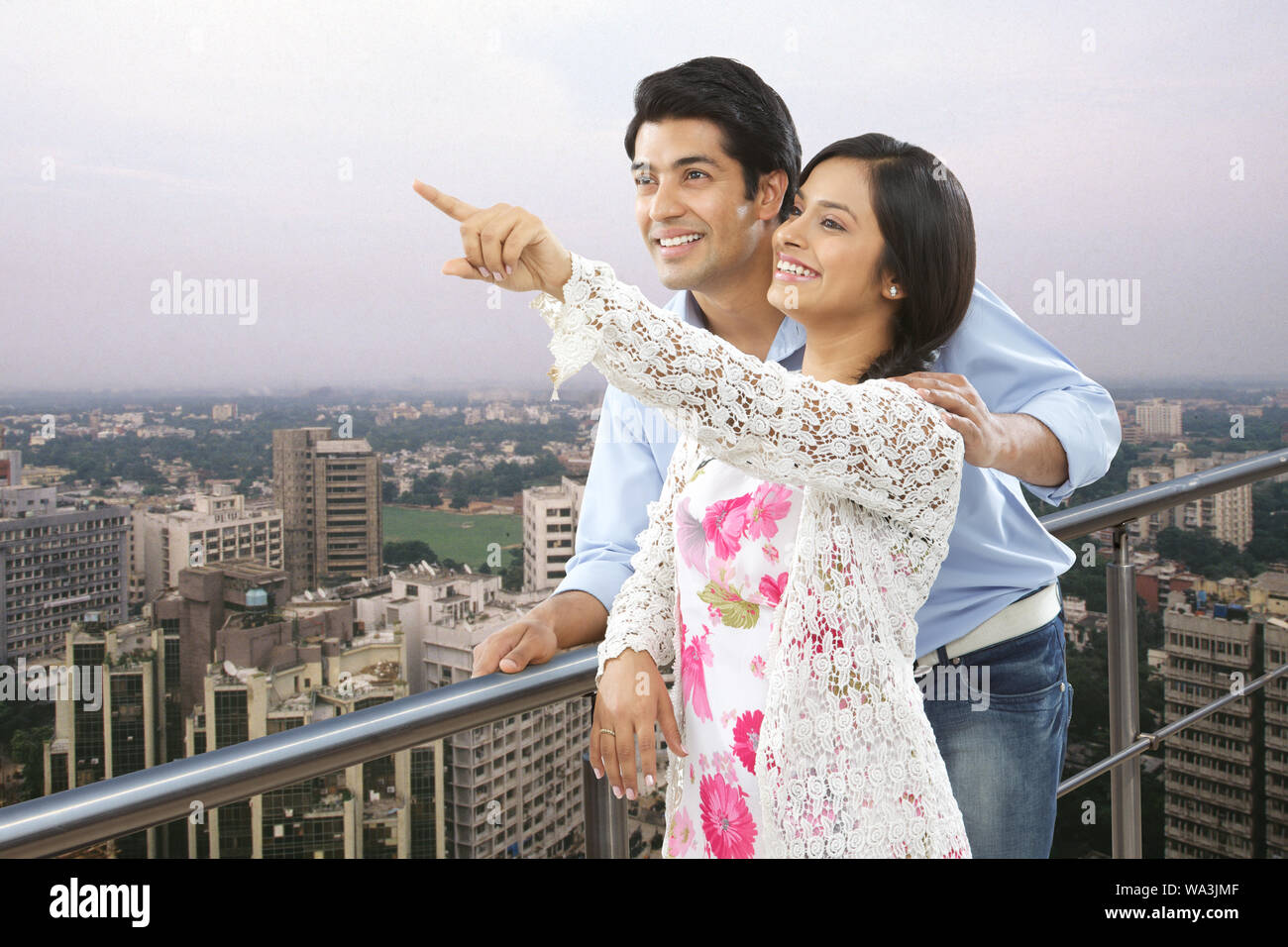 Young woman standing in a balcony and showing something to her husband Stock Photo