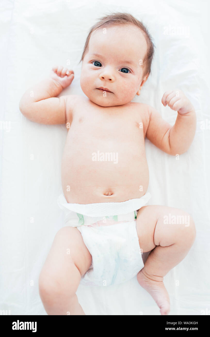 Funny little baby wearing a diaper lying on a white sheet. Child after