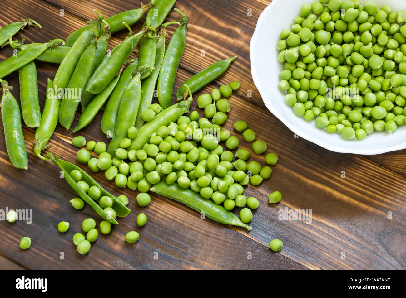 Natural organic homegrown products. Fresh green peas in a glass jar and scattered peeled beans on dark wooden table. White bowl with peeled peas. Top Stock Photo