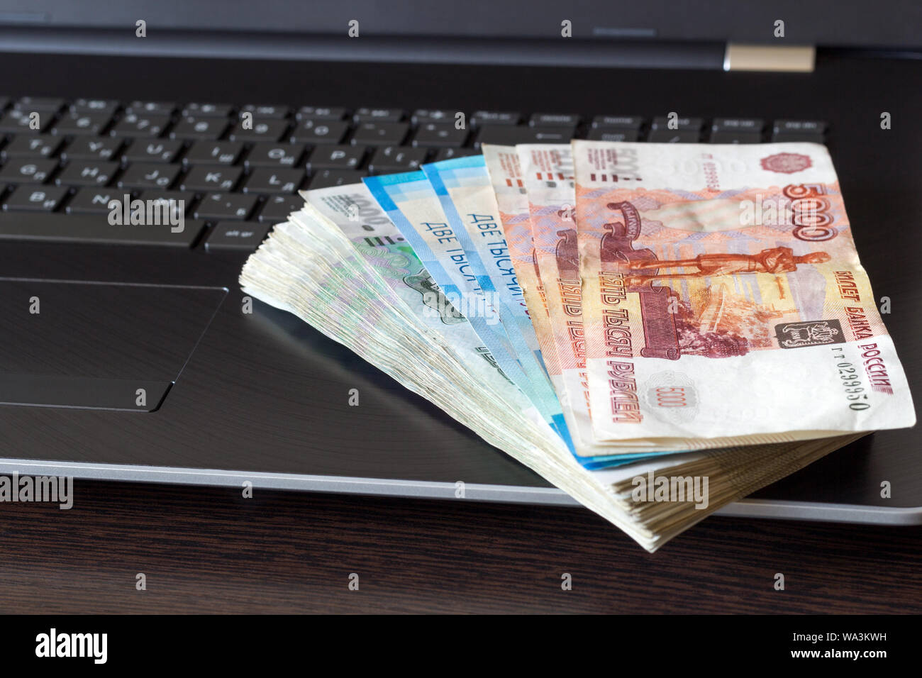 Stack of russian rubles lay on laptop keyboard. Dark brown wooden table with copy space. Payments for computer work concept. Top angle view. A banknot Stock Photo