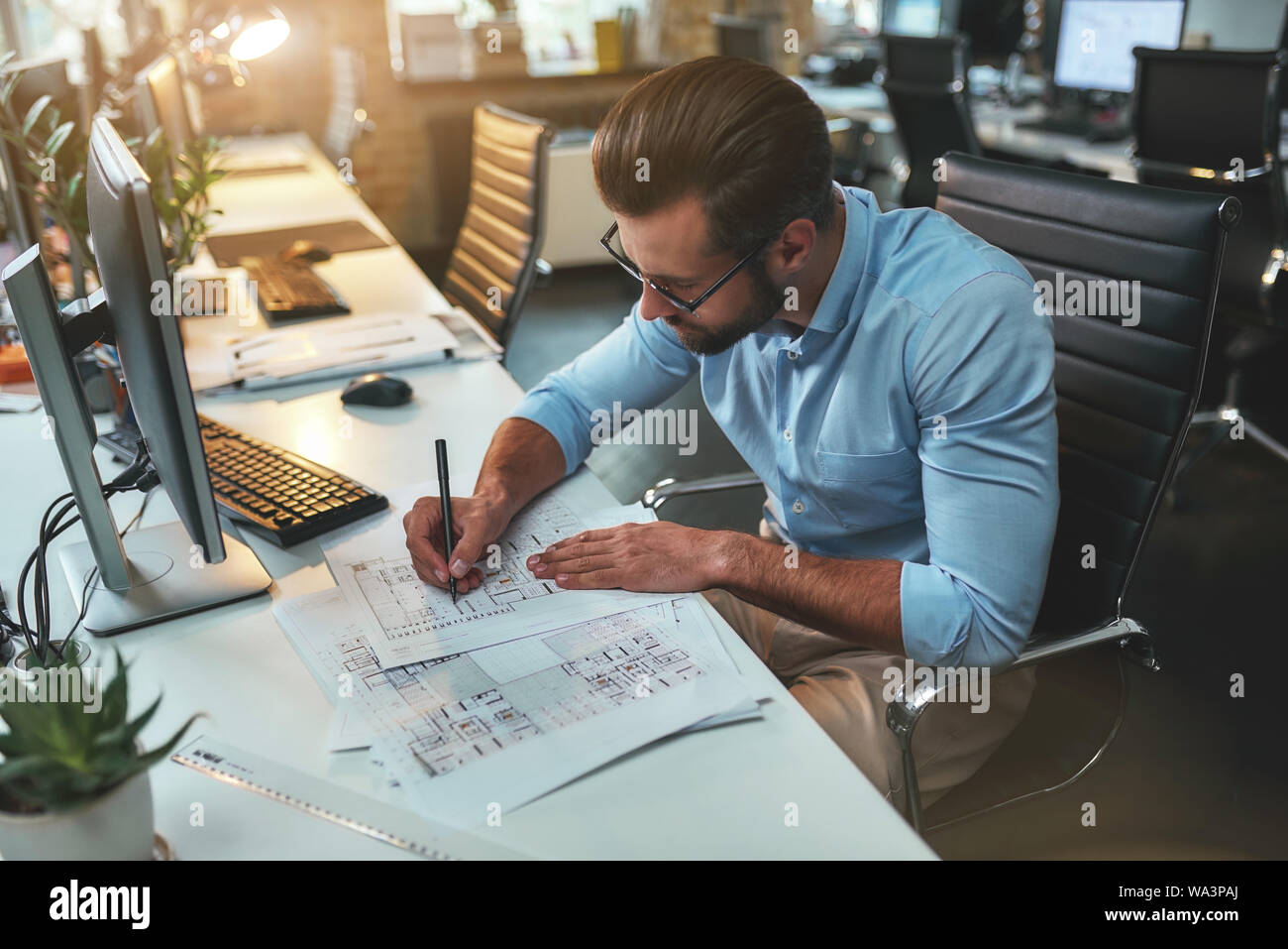 Architectural project. Successful busy bearded man in eyeglasses and formal wear drawing something while working in the office. Engineer. Construction plan Stock Photo