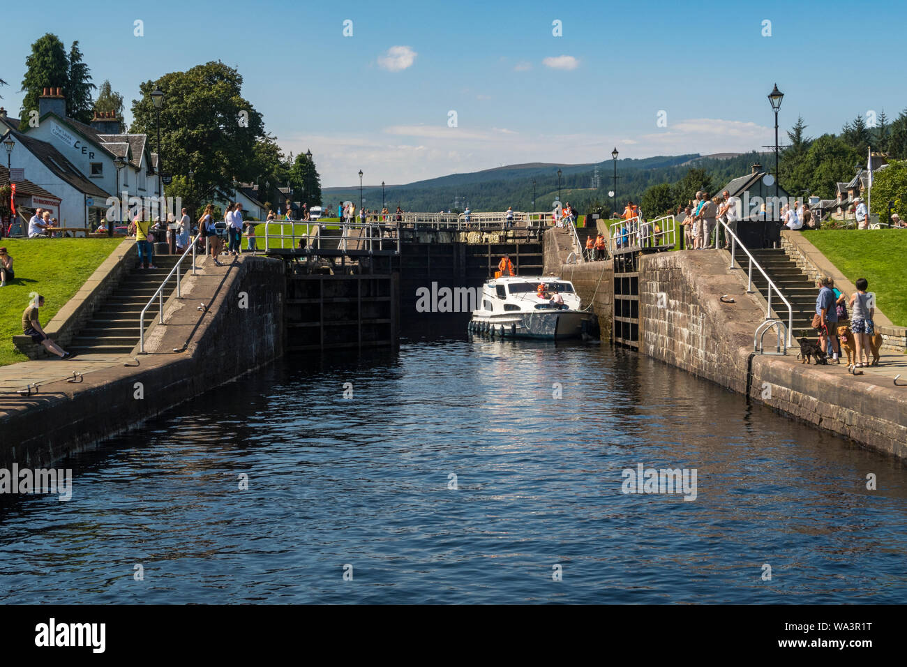 A boat makes its way through locks on the Caledonian Canal at Fort Augustus near Loch Ness in Scotland on a sunny day, watched by tourists. Stock Photo