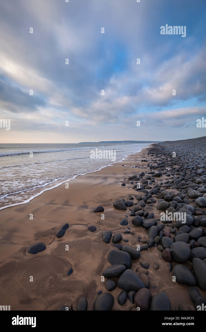 portrait view of westward Ho! beach in North Devon near sunset. You can see the waves wash over the sand of the beach. Stock Photo
