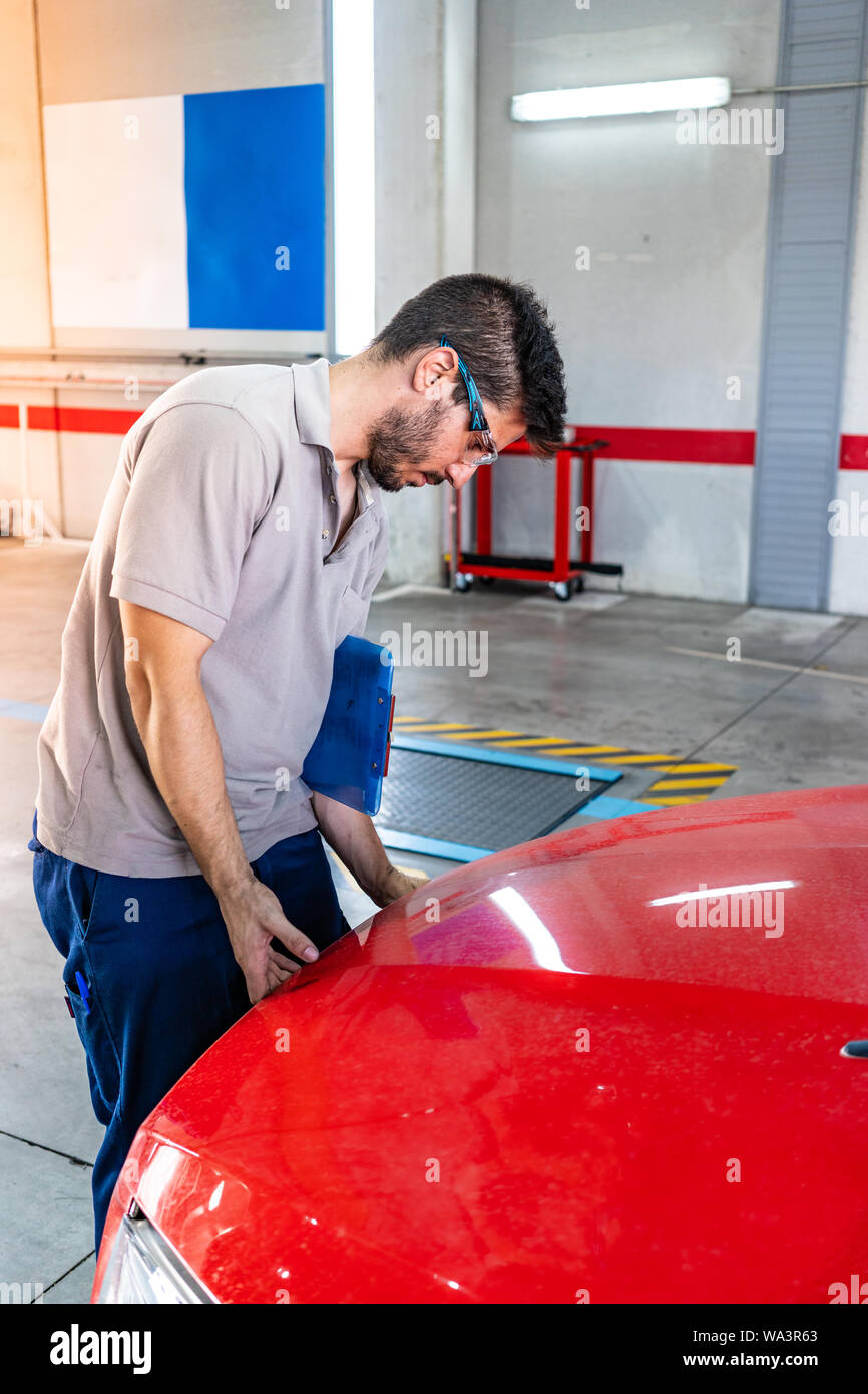 Technician with safety glasses opening the hood of a red car during a vehicle inspection Stock