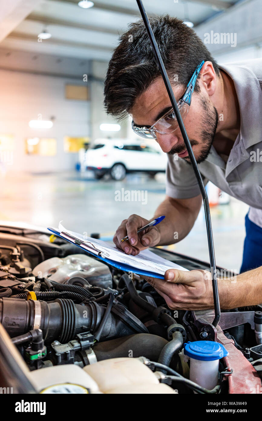 Technician with safety glasses checking the engine of a red car during a vehicle inspection