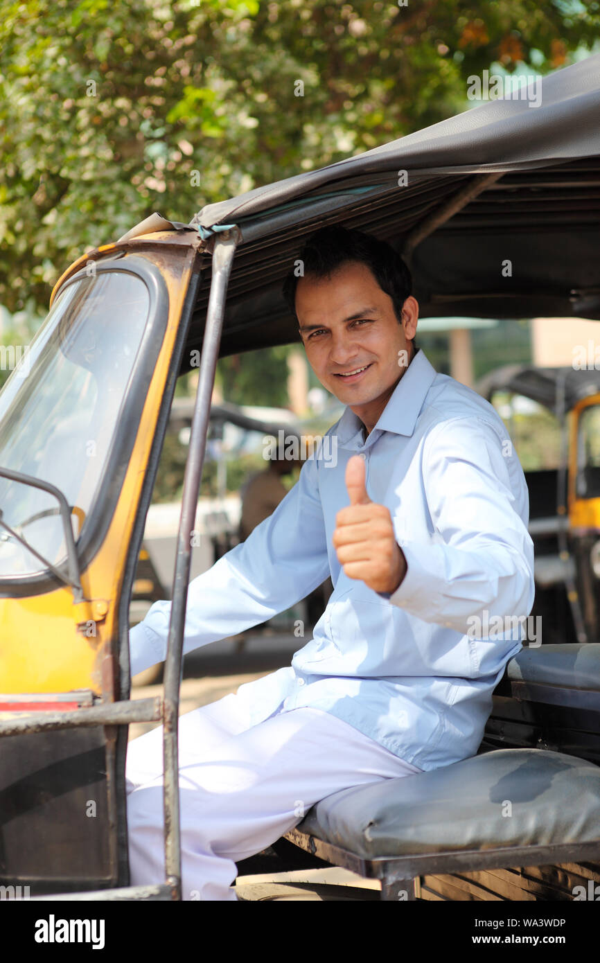 Auto driver driving an auto rickshaw and showing thumbs up sign Stock Photo
