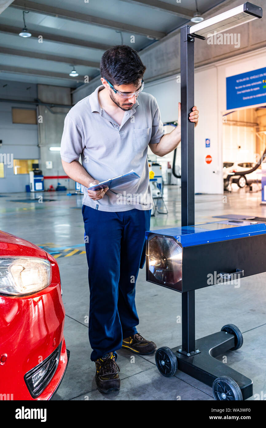 Technician with safety glasses checking the head lights of a red car during a vehicle inspection