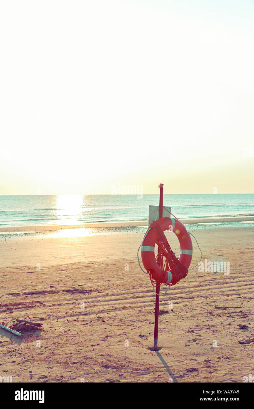 Lifebuoy on the beach by the sea. Sunset and sun flare. Tinted photo Stock Photo