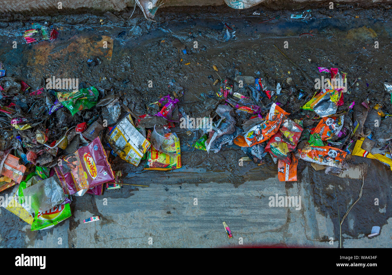 packaging waste in a muddy street in Asia Stock Photo