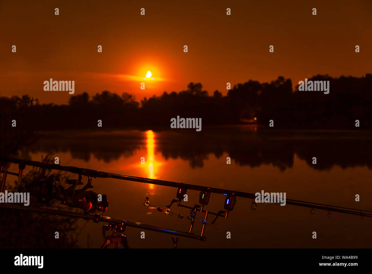 Fishing spinning angling rods with Fishing Bite Alarm and LED Lights on standing pod in the beach lake. Night Fishing, Carp Rods, Moon over lake Stock Photo