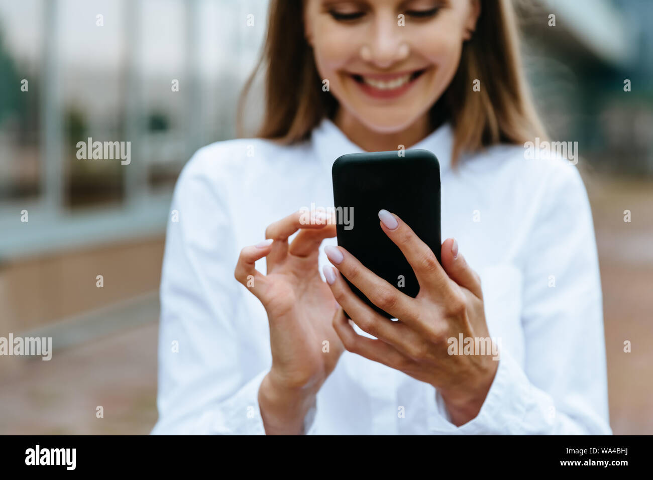 Cropped view of businesswoman using smartphone. Successful female entrepreneur checking email on smartphone. Female texting message. Office building Stock Photo