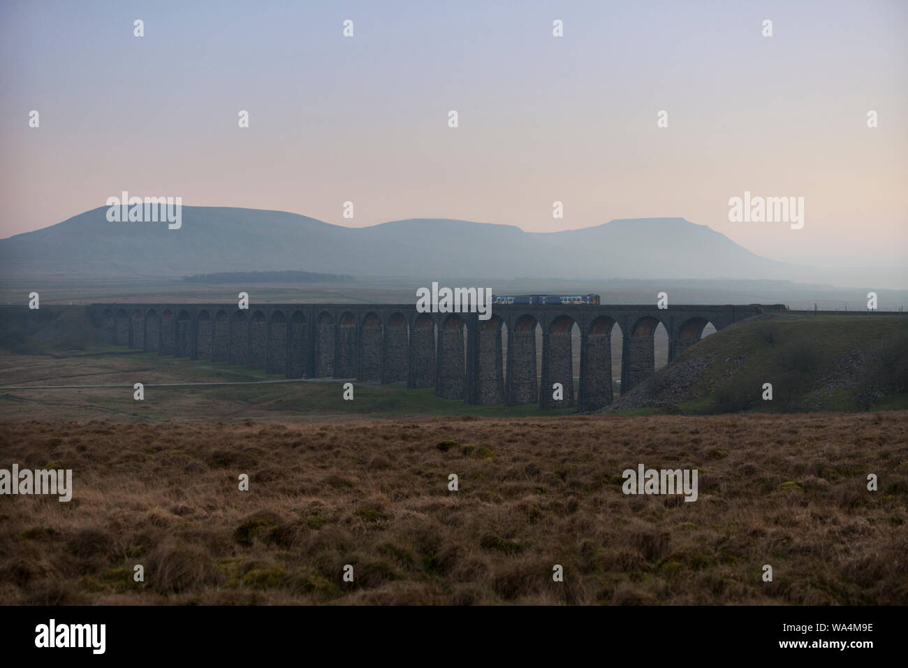Arriva Northern rail class 158 sprinter train crossing Ribblehead viaduct at sunset with Ingleborough behind Stock Photo