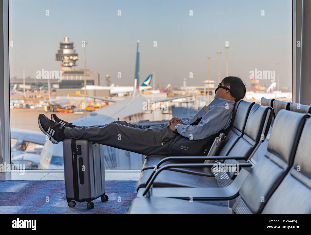 Hong Kong Airport, Hong Kong - October 29th, 2018: A young woman sleeping on a seat at the Hong Kong airport, resting his feet on his suitcase. Stock Photo