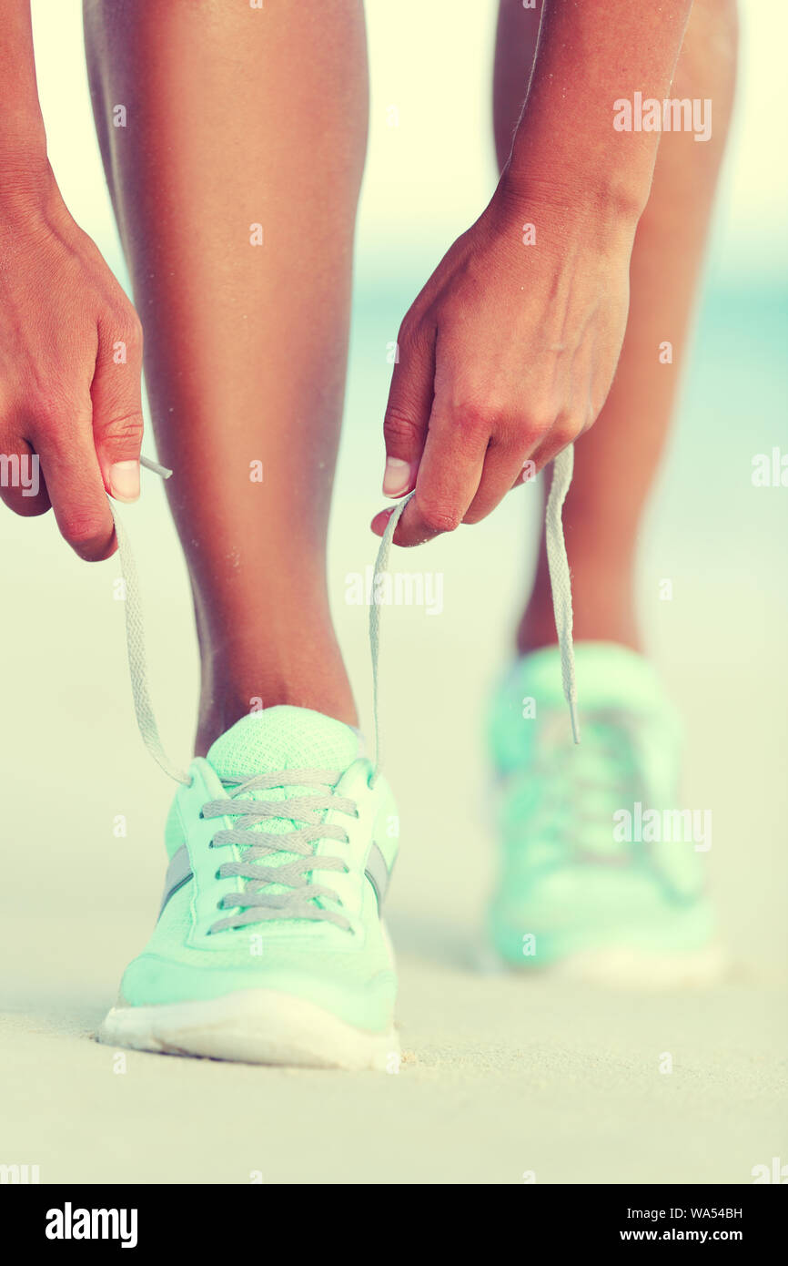 Active life runner girl tying running shoes laces. Healthy lifestyle woman runner tying running shoes laces for cardio training on beach at sunset. Female athlete exercising. Stock Photo