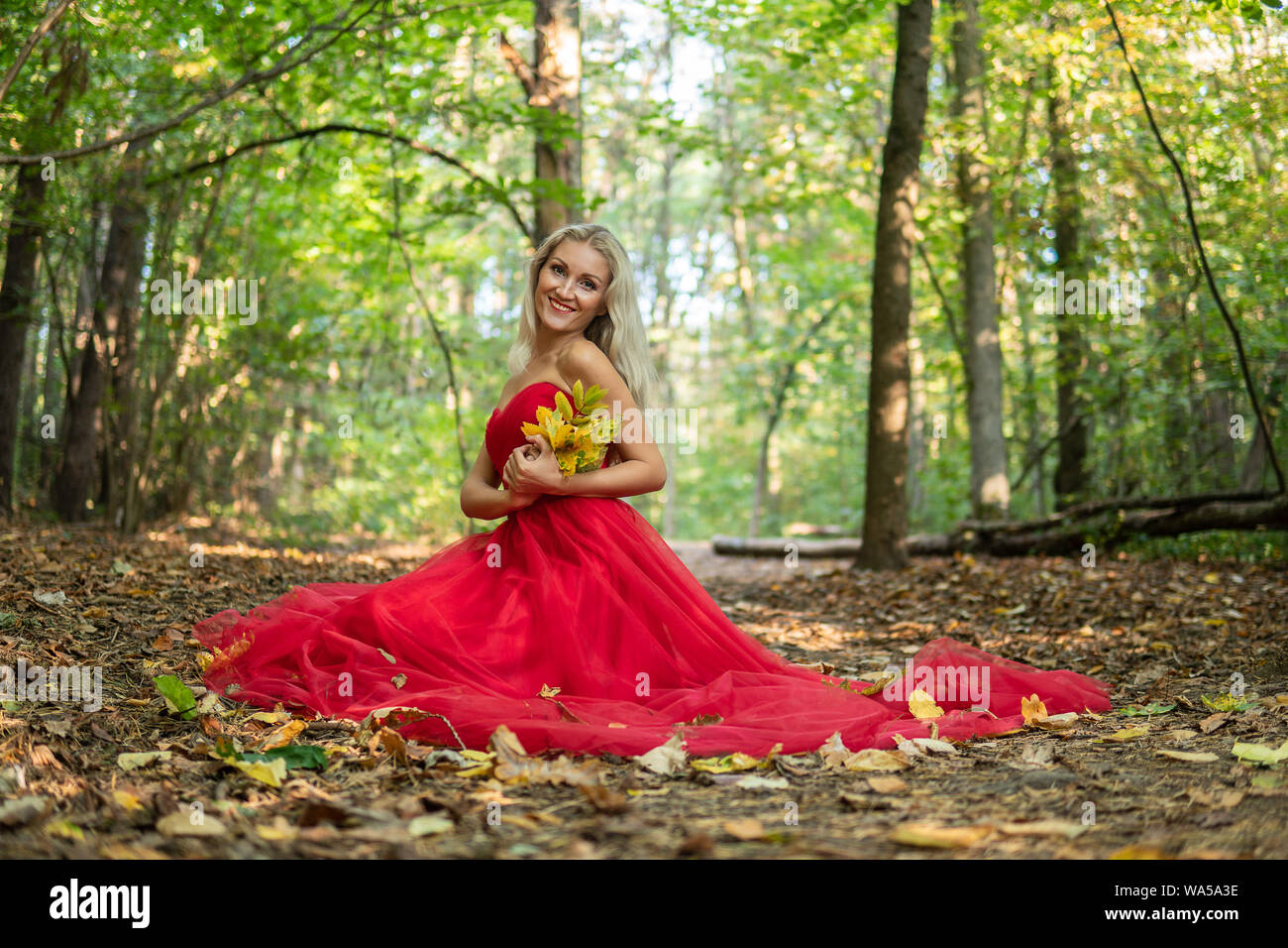 Surprised beautiful young woman in red dress is pointing and shouting. Three quarter length studio shot on gray background. Stock Photo